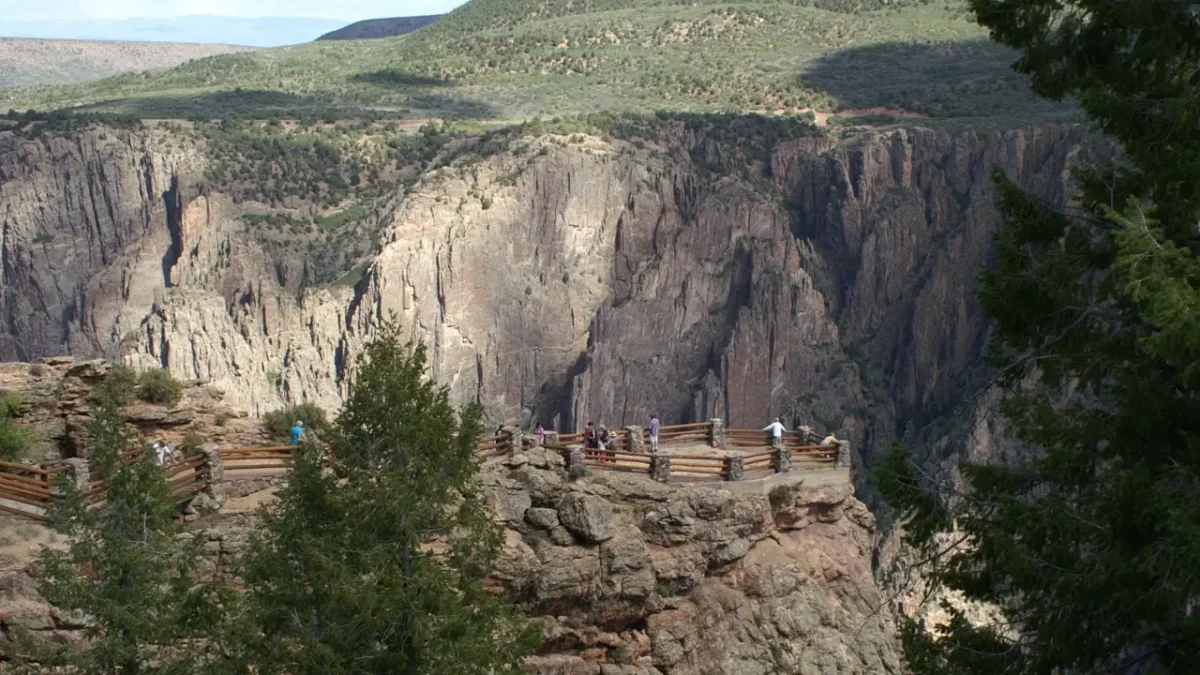 Panoramic view of Black Canyon of the Gunnison National Park from the South Rim overlook with visitors enjoying the dramatic cliffs and canyon scenery.