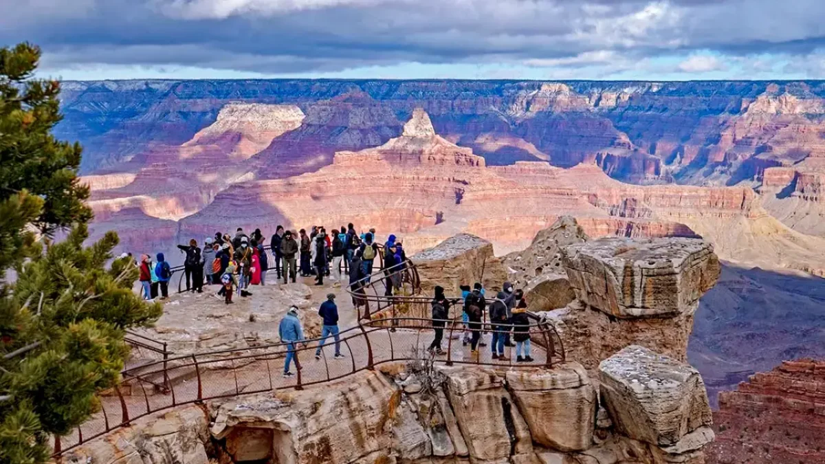 Visitors gathered at Mather Point overlook in Grand Canyon National Park, admiring the vast red rock cliffs and layered canyon landscape under a dramatic sky.