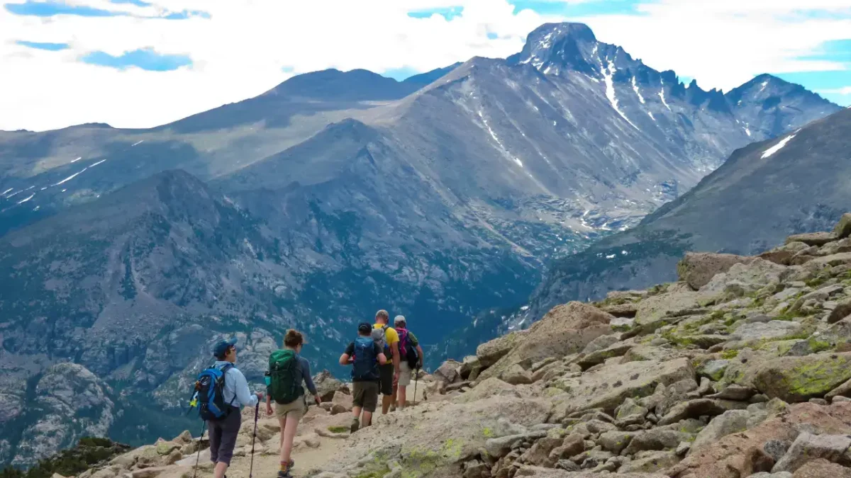 Hikers walking along a rocky alpine trail with sweeping views of peaks and valleys in Rocky Mountain National Park.