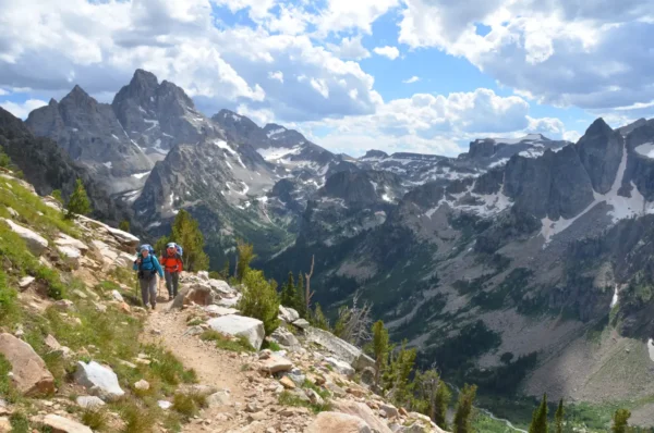 Two hikers on a mountain trail overlooking the rugged Teton Range in Grand Teton National Park.