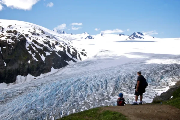 Visitors overlooking a glacier in Kenai Fjords National Park, Alaska, with snow-covered mountains and the Harding Icefield in the background.